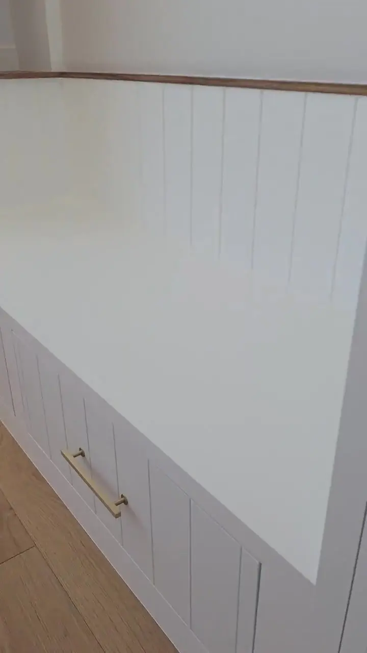 Walkthrough of a finished built-in bench with vertical panelling and a sprayed white drawer bank set beneath a solid wood shelf.