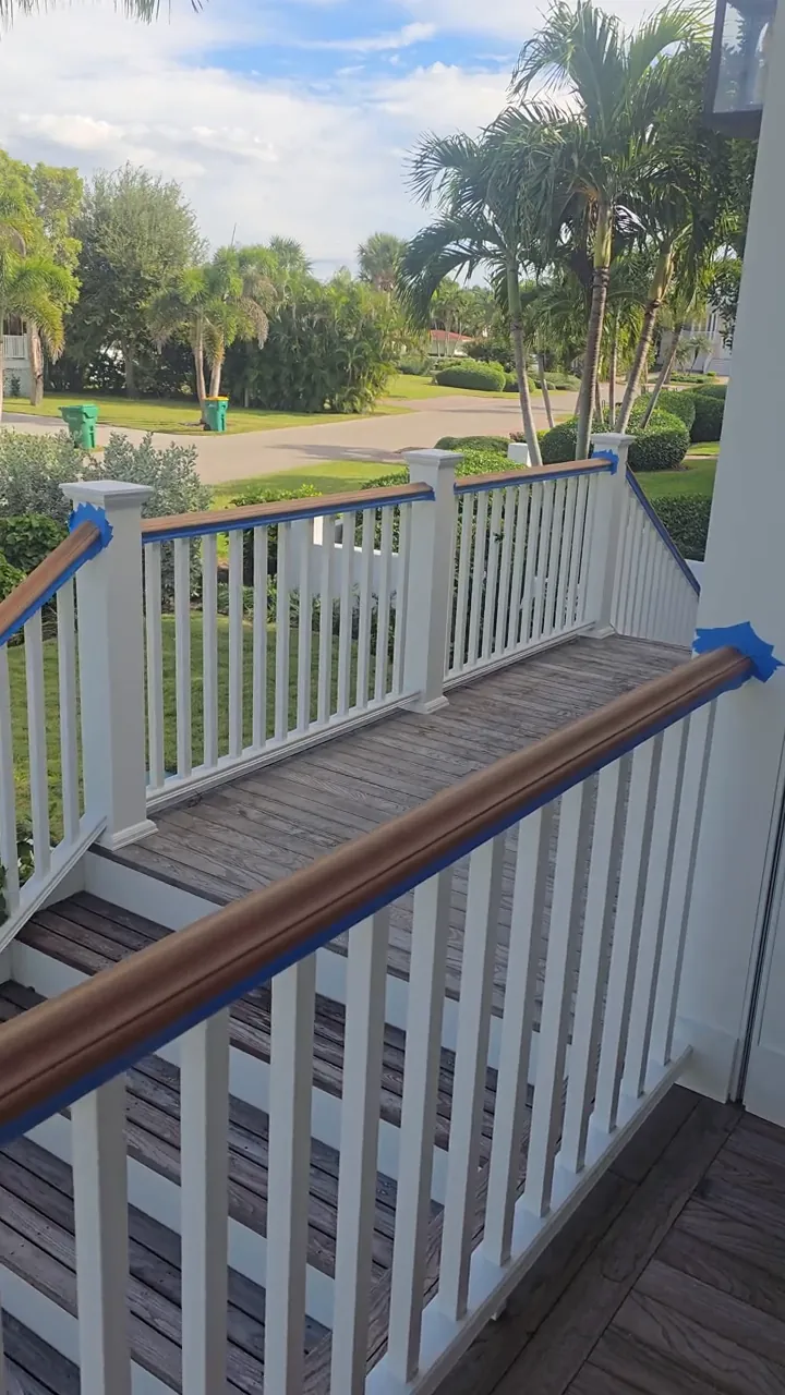 A deck handrail carrying a fresh coat of mahogany stain over hand-painted white balusters, masked at the joint so the two finishes meet clean.