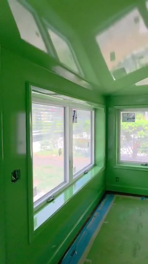 Walkthrough of a room finished throughout in high-gloss green enamel — walls, ceiling, window returns and door — with the light coming back off every surface.